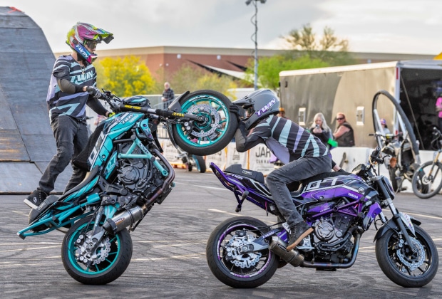 Two Twinstunts Riders Performing A Coordinated Motorcycle Wheelie Stunt During A Live Show