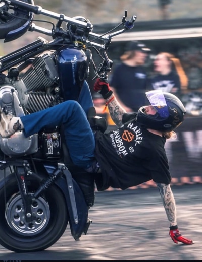 Jonny Tompkins performing a precise hand-drag stunt on a Harley-Davidson motorcycle at a live show