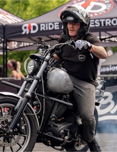 Jonny Tompkins Performing A Precise Hand-Drag Stunt On A Harley-Davidson Motorcycle At A Live Show